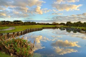 A photo of a pond reflecting the sky and clouds next to a golf course.