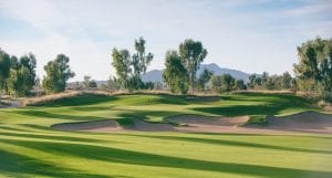A photo of a golf course with trees and mountains in the background.