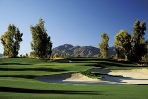 An immaculate golf course with trees and mountains in the background.