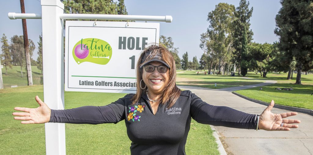Azucena Maldonado of Latin Golfers Association in front of a golf hole sign for the Latina Golfers Association