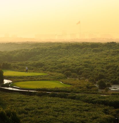 Aerial view golfer tees off on hole 16 at Al Zorah Golf Club surrounded by mangroves